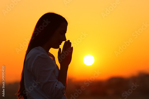 Backlight of a woman praying at sunset
