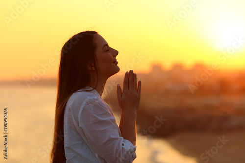 Profile of a woman praying at sunset