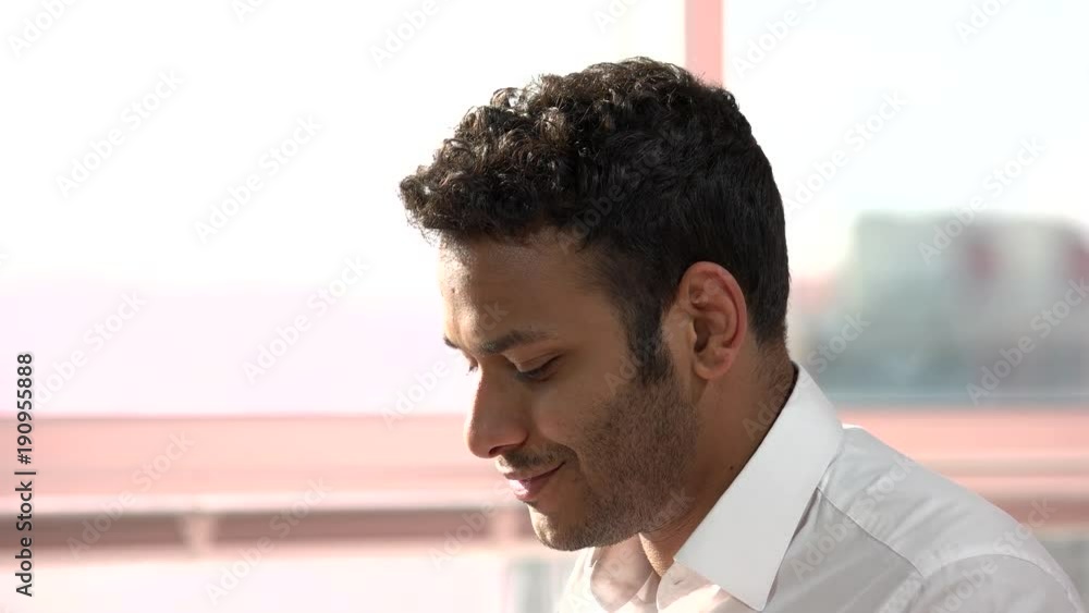 Smiling indian man face while typing. Indian stubbed face starting to laugh while using computer in office, side view. Smiling indian man face while typing. Indian stubbed face starting to laugh while using computer in office, side view.