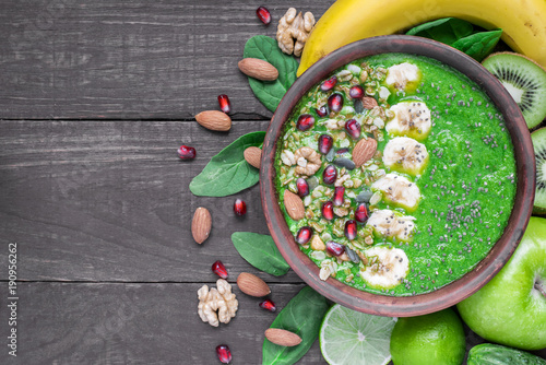 Green fruit and vegetable smoothie bowl topped with granola, banana, pomegranate, pumpkin and chia seeds