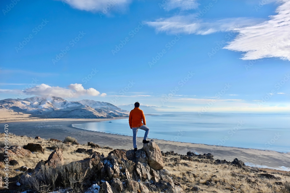 Fototapeta premium Great Salt Lake and Antelope Island in a winter day. Man hiker on a cliff abover the lake enjoying the scenic views. Salt Lake City. Antelope Island State Park. Utah. United States.