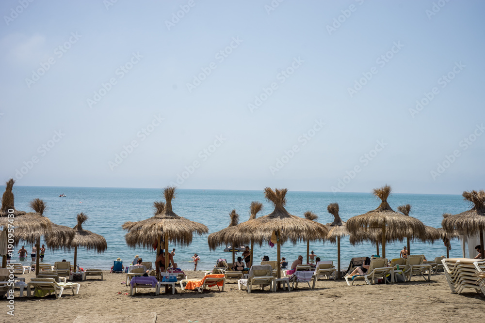Holiday scene at the malagueta beach with palm roofs on a summer day with the ocean in the background in Malaga, Spain, Europe Holiday scene at the malagueta beach with palm roofs on a summer day with the ocean in the background in Malaga, Spain, Europe