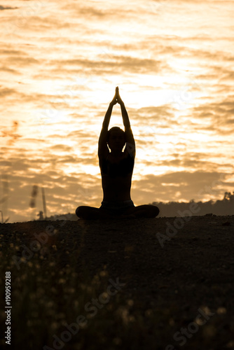 Silhouette young woman practicing yoga on the mountain at sunset.