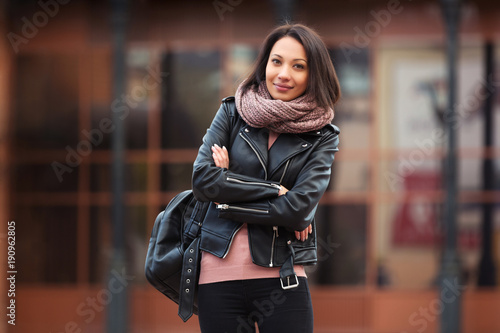 Young fashion woman in black leather jacket walking in city street