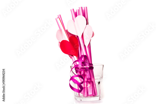 valentine's day holiday. bright pink drinking straws with hearts and a pink ribbon in a glass isolated on white.bright sipping straws for party or birthday