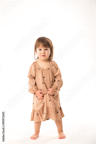 Cute little girl in beige dress isolated on white background. Portrait of happy little girl on white background. Sweet girl with curly hair.