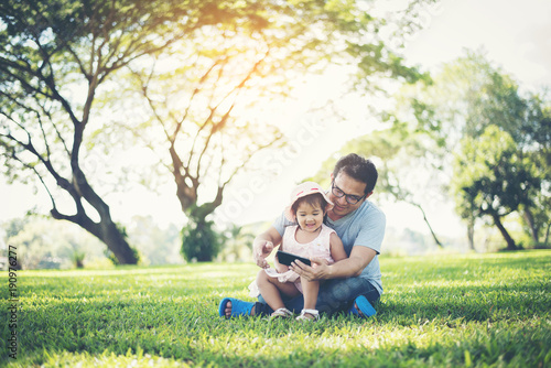 Father and daughter smiling using smartphone in the park © Johnstocker