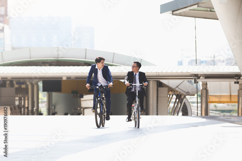 Asian handsome young businessmen talking while riding bicycles in city
