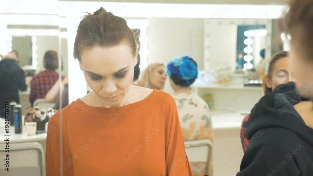 Young beautiful girl draws shadows on the eyelids. She is standing in front of the mirror and doing makeup. In a beauty salon Young beautiful girl draws shadows on the eyelids. She is standing in front of the mirror and doing makeup. In a beauty salon
