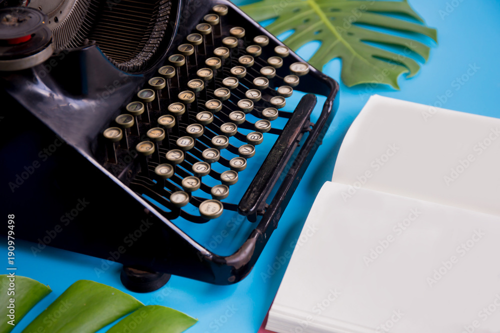 Open book with blank paper pages decorated with typewriter and leaves