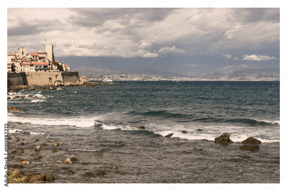 Vintage Style with waves at stone coast with mediterranean village in background