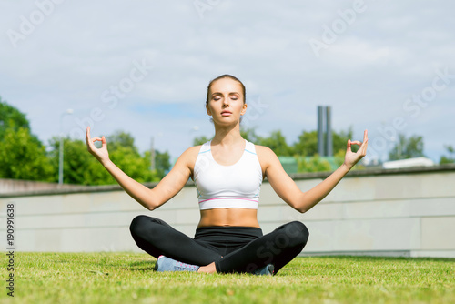 Young, fit and sporty woman doing yoga exercise meditation in the park. Fitness, sport, urban and healthy lifestyle concept.