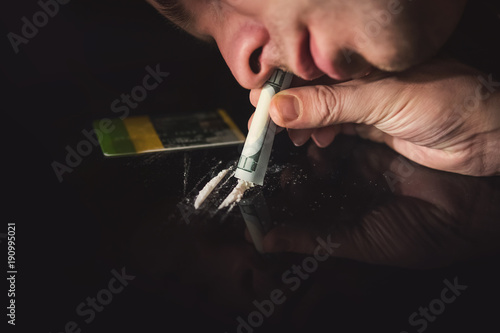 Fotografie Young addict snorting white cocaine through