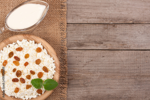 Cottage cheese in bowl with sour cream and raisins on old wooden background with copy space for your text. Top view