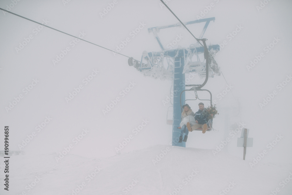 Young pretty pair of lovers. Winter. Date. A couple of passions rise on a funicular in a snowy day on the top of the mountain Young pretty pair of lovers. Winter. Date. A couple of passions rise on a funicular in a snowy day on the top of the mountain