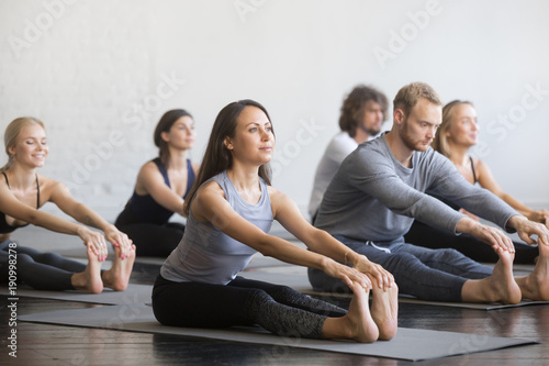 Obraz na plátně Group of young sporty people practicing yoga lesson with instructor, sitting in