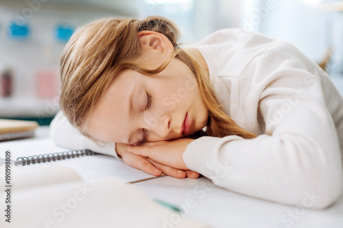 Having a rest. Adorable fair-haired little girl sleeping over her books while sitting at the table and doing homework