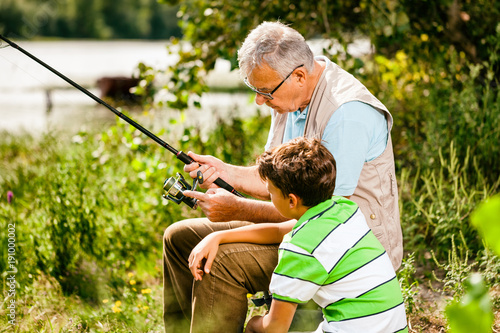 Grandfather and grandson are fishing on sunny day. 