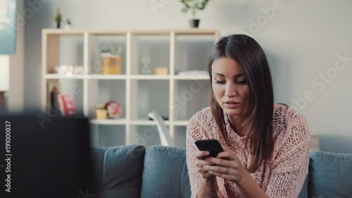 Beautiful Ukrainian girl dialing mobile number from TV screen on cellphone. Smiling girl looking aside and calling television store.