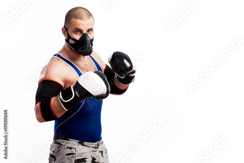 Young sportive man in blue tights,black elbow, black and white boxing gloves and training mask boxing on a white isolated background