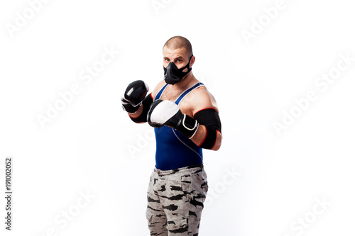 Young sportive man in blue tights,black elbow, black and white boxing gloves and training mask boxing on a white isolated background