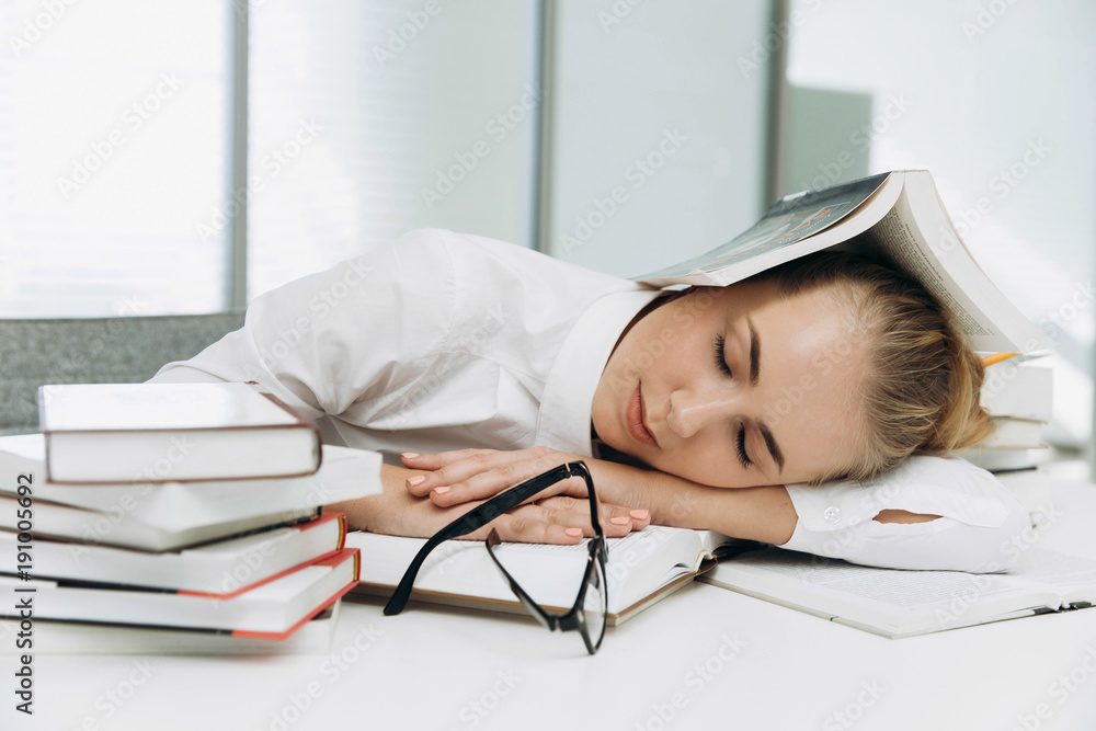 Tired student sleeps on the books in the library Tired student sleeps on the books in the library