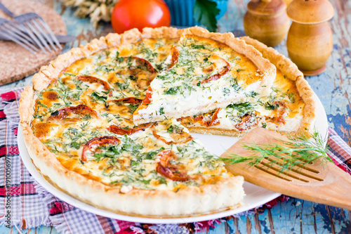 Sliced homemade french quiche pie with tomato, cheese and herb on a plate.