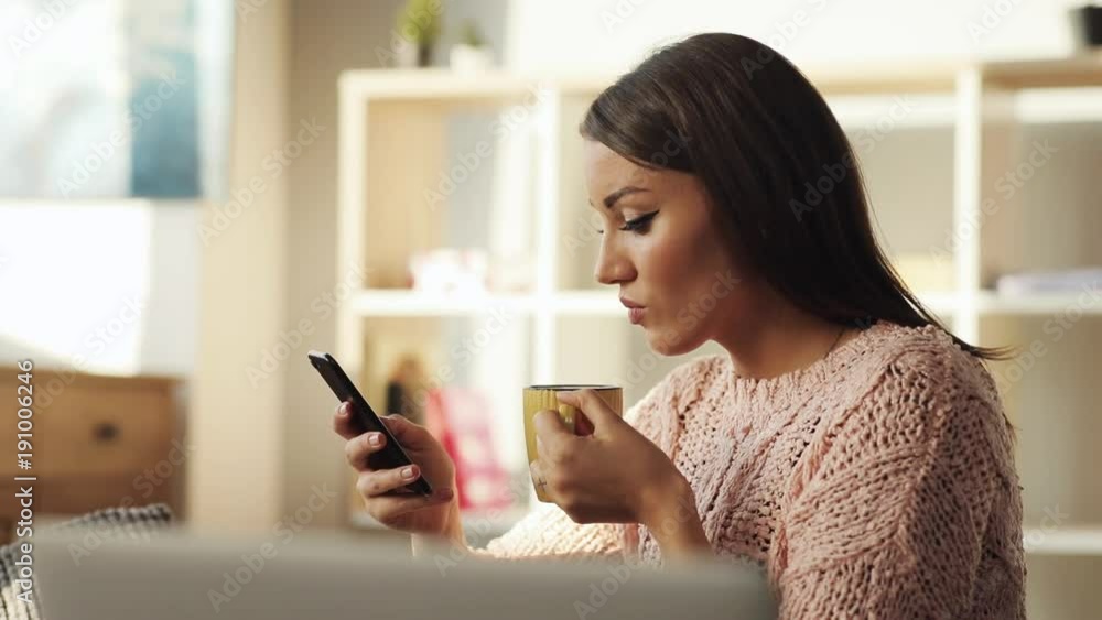 Lovely young Ukrainian woman sitting on couch, drinking tea from yellow cup. Attractive Caucasian girl using smartphone, messaging, browsing. Indoors. Profile. Lovely young Ukrainian woman sitting on couch, drinking tea from yellow cup. Attractive Caucasian girl using smartphone, messaging, browsing. Indoors. Profile.