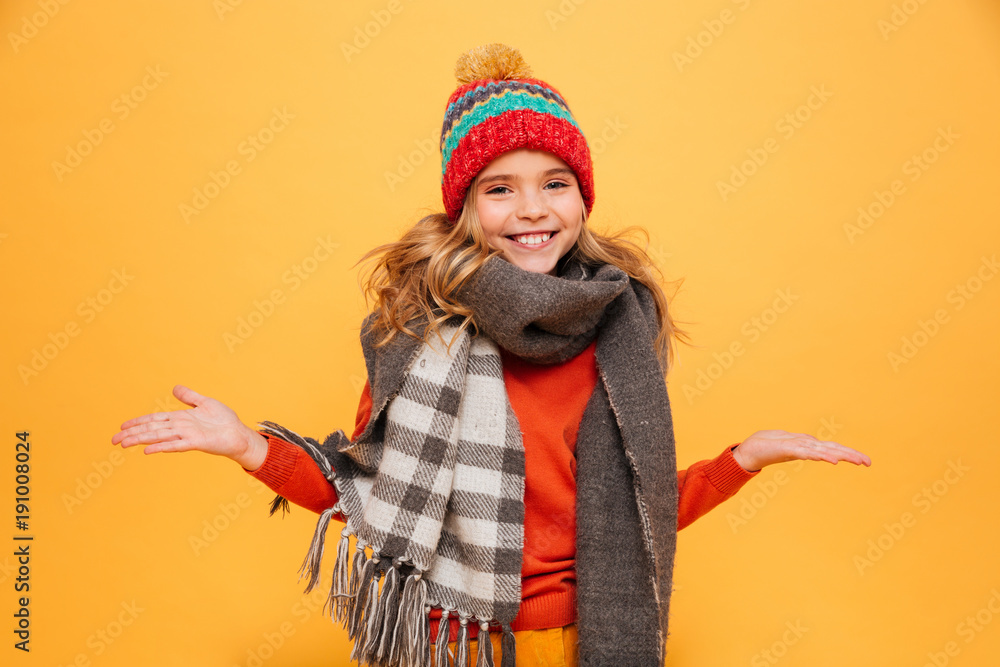 Happy girl in sweater, scarf and hat shrugs her shoulders