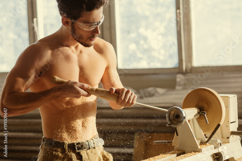 Turner working on a lathe in the workshop. Male hand carved wooden blank photo