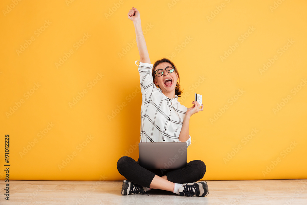 Φωτογραφία Young woman screaming in happiness while sitting in lotus pose on the floor usin