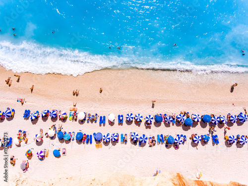 Top down view of a beach with tourists suntbeds and umbrellas with sand beach and clear blue water in Greece