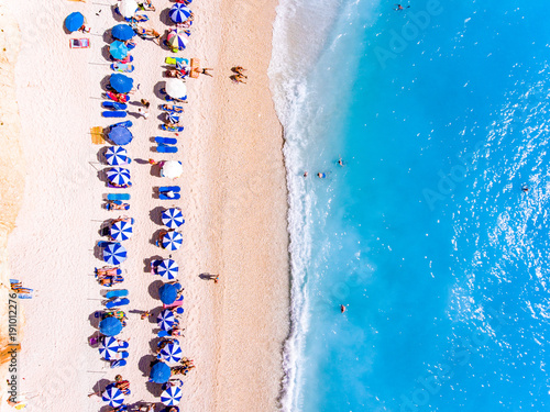 Top down view of a beach with tourists suntbeds and umbrellas with sand beach and clear blue water in Greece