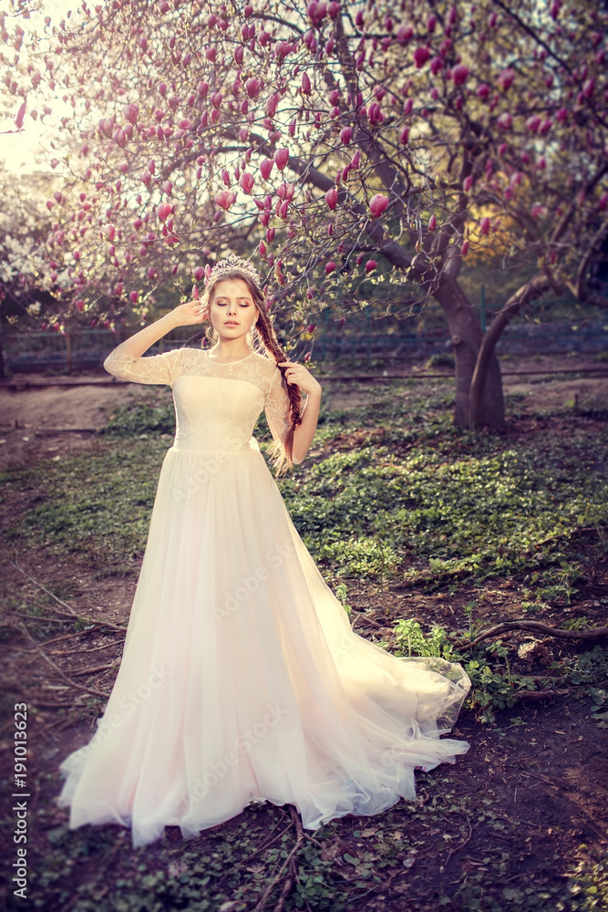 Beautiful bride posing near magnolia tree. Woman in white dress in spring garden.