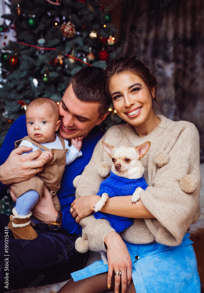 The mother,father,dog and baby sitting near Christmas Tree