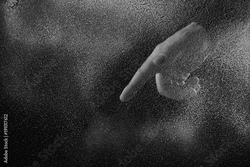 cropped shot of person pointing down with finger through frosted glass in darkness