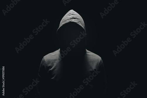 faceless man in hoodie standing isolated on black photo