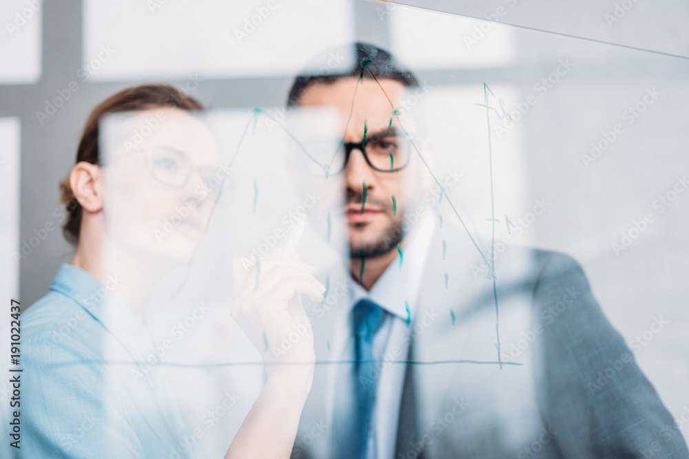 confident businesspeople drawing graphs on glass presentation board confident businesspeople drawing graphs on glass presentation board