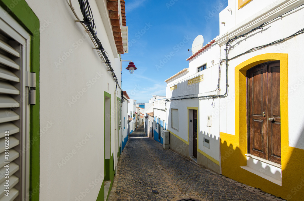 Narrow street of Salema village. Ocean view and whitewashed houses of the small authentic fishing village. Architecture details. Faro, Algarve, Southern Portugal. Narrow street of Salema village. Ocean view and whitewashed houses of the small authentic fishing village. Architecture details. Faro, Algarve, Southern Portugal.