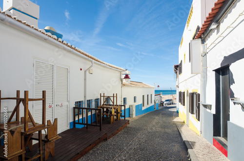 Narrow street of Salema village. Ocean view and whitewashed houses of the small authentic fishing village with a lots of small cafes, bars and sea food restaurants. Faro, Algarve, Southern Portugal.