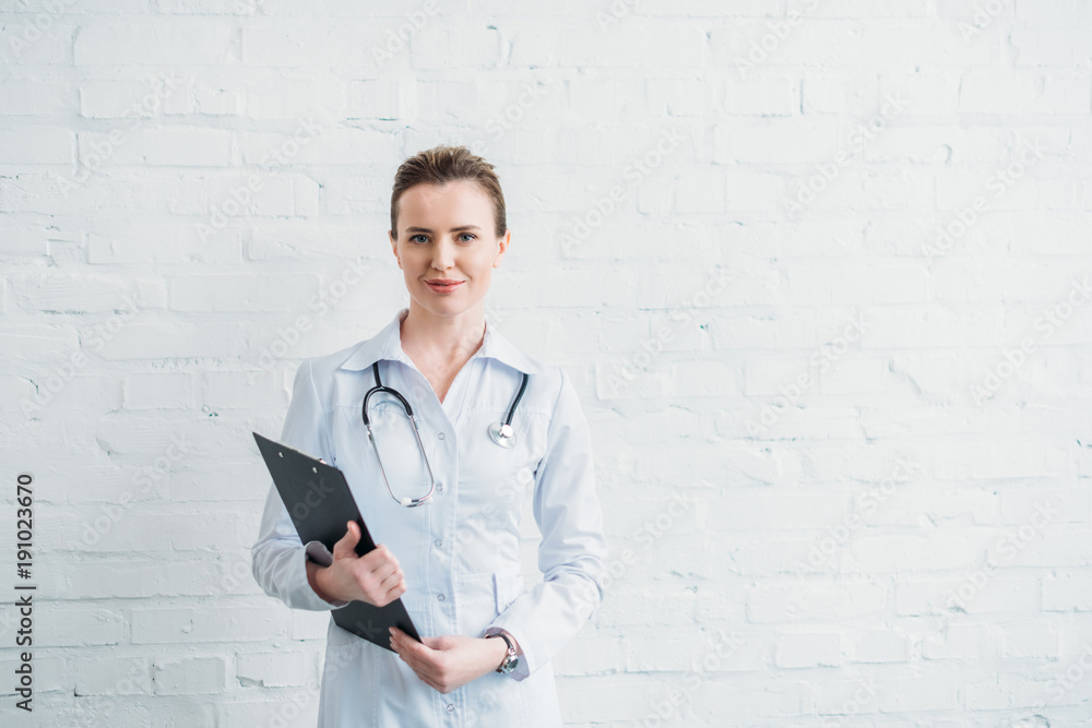 beautiful female doctor with clipboard in front of white brick wall beautiful female doctor with clipboard in front of white brick wall