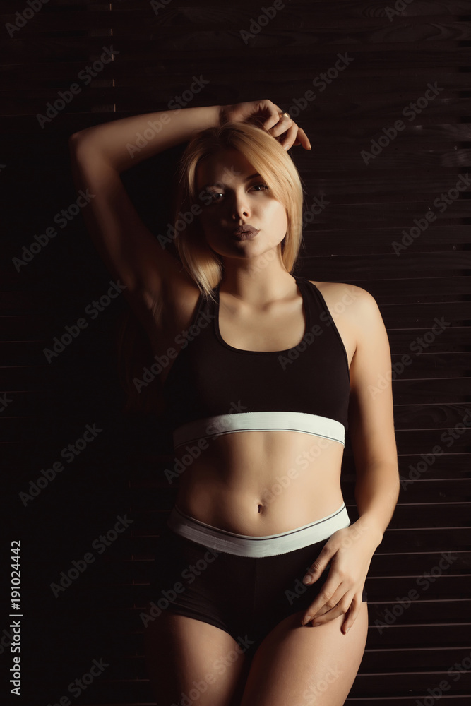 Fototapeta premium Adorable blonde woman in sport underwear posing in studio with shadow