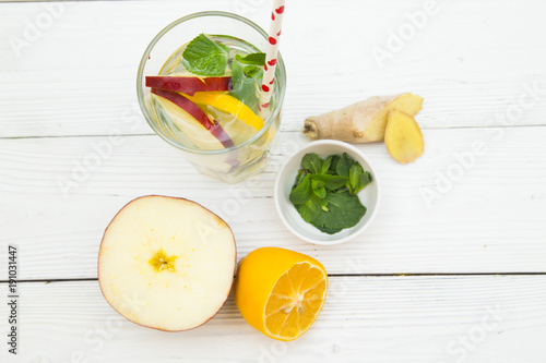 A glass of detox water with sleces of fresh apple, lemin ginges and spinach with ingredients on white wooden table, top view