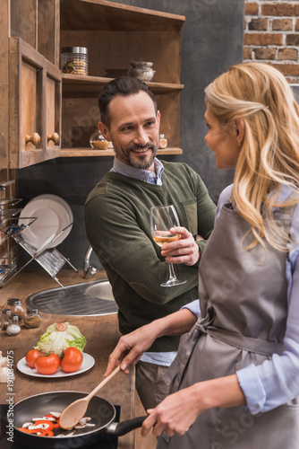 husband standing with wine near wife while she cooking at kitchen