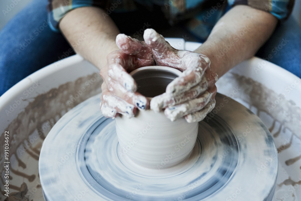 Close-up of hands doing a pot or a vase in ceramic studio, craft working process with clay potter's wheel