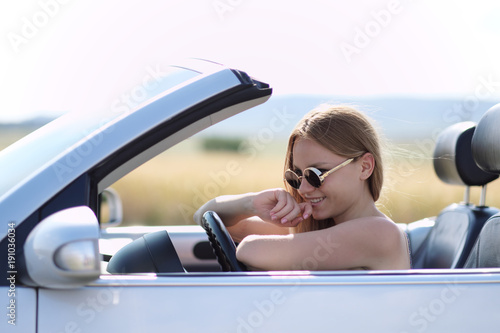 Girl driving a convertible car in a summer poppy field
