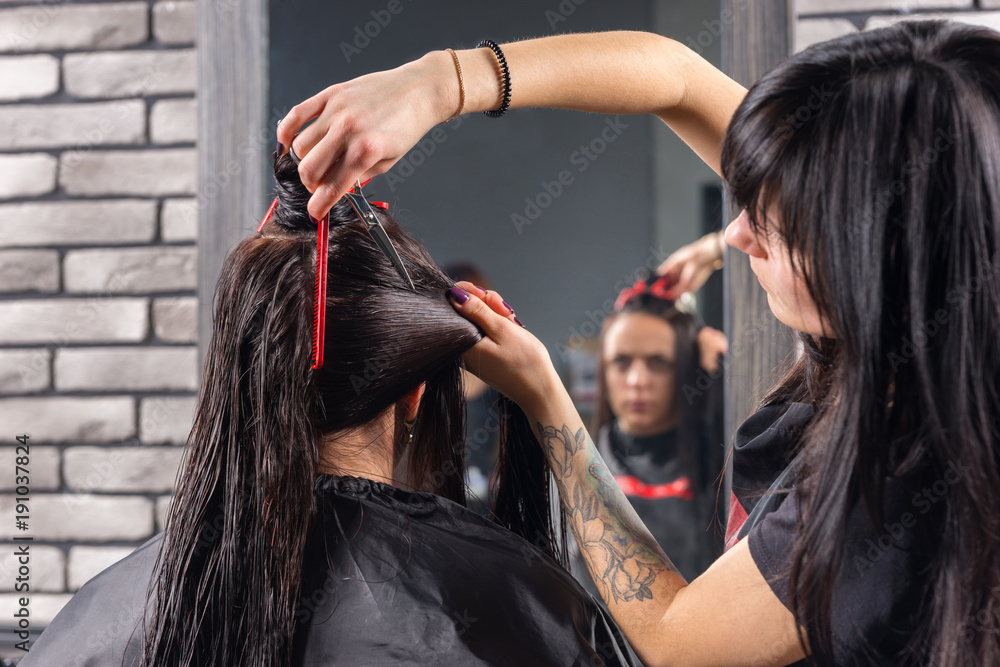 Naklejka premium Close up female stylist with tattooed hands cutting and modeling brown hair by scissors and comb