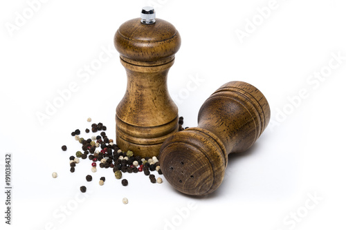 Wooden salt shaker and pepper mill surrounded by diverse peppercorns on white background. Checkmate metaphor.