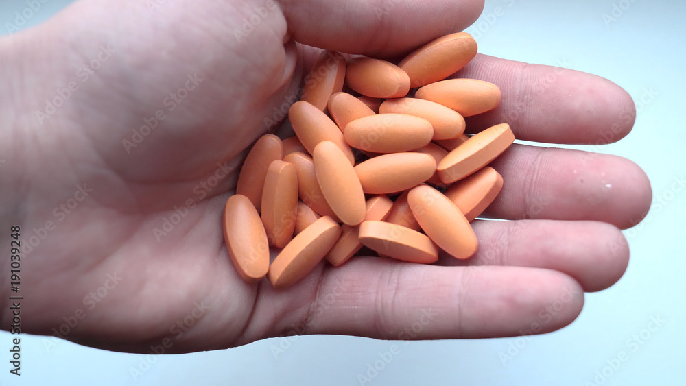 Holds orange capsules, pills or vitamins scattered on a white table. Holds orange capsules, pills or vitamins scattered on a white table.