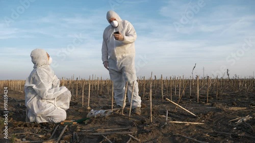 Slow motion footage of ecology specialists in white protection clothes observing and analyzing contaminated landscape, entering data on smartphone